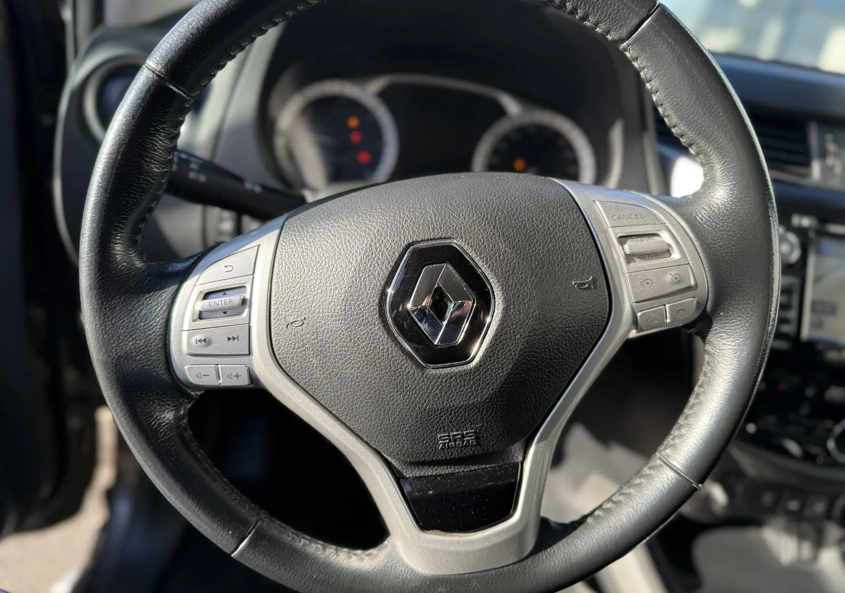 Gros plan sur le volant en cuir noir du Renault Alaskan 2018, avec commandes intégrées et logo central brillant.