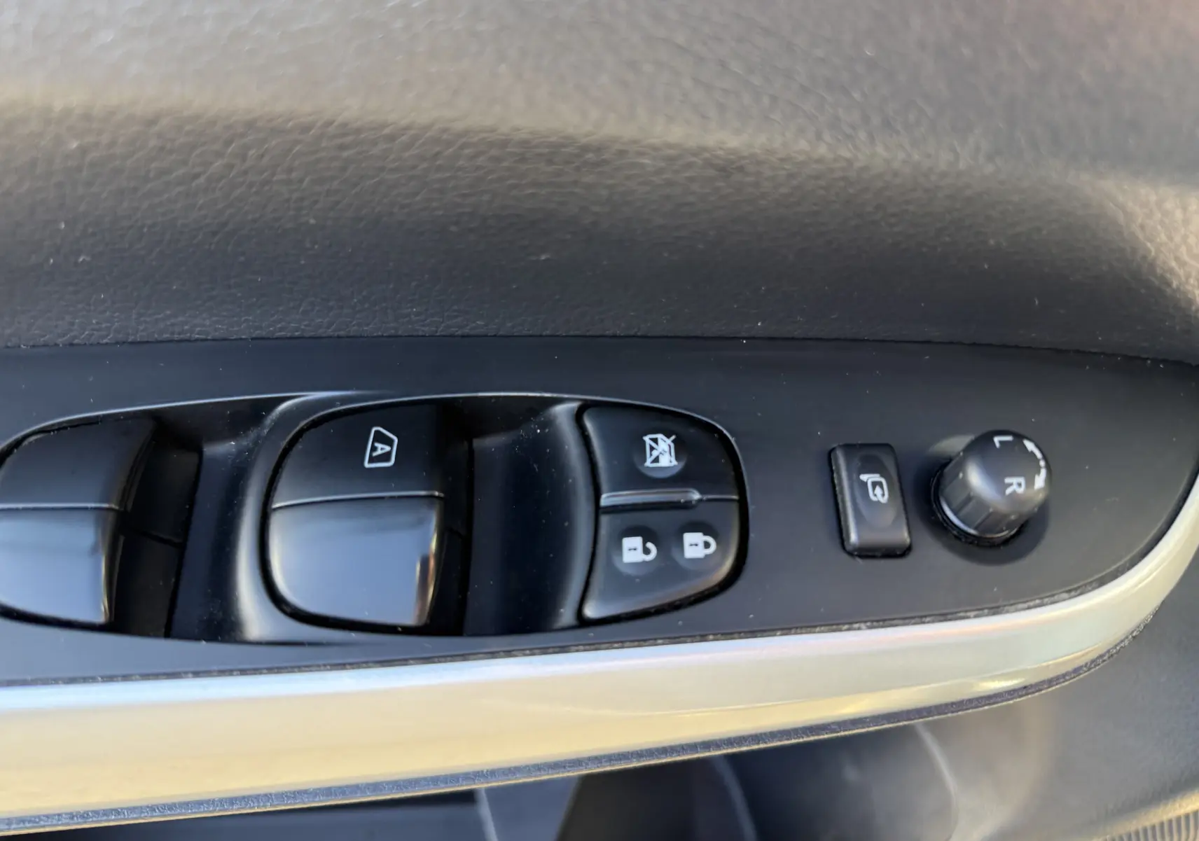 Gros plan sur les commandes de lève-vitres et réglage des rétroviseurs côté conducteur du Renault Alaskan brun 2018.