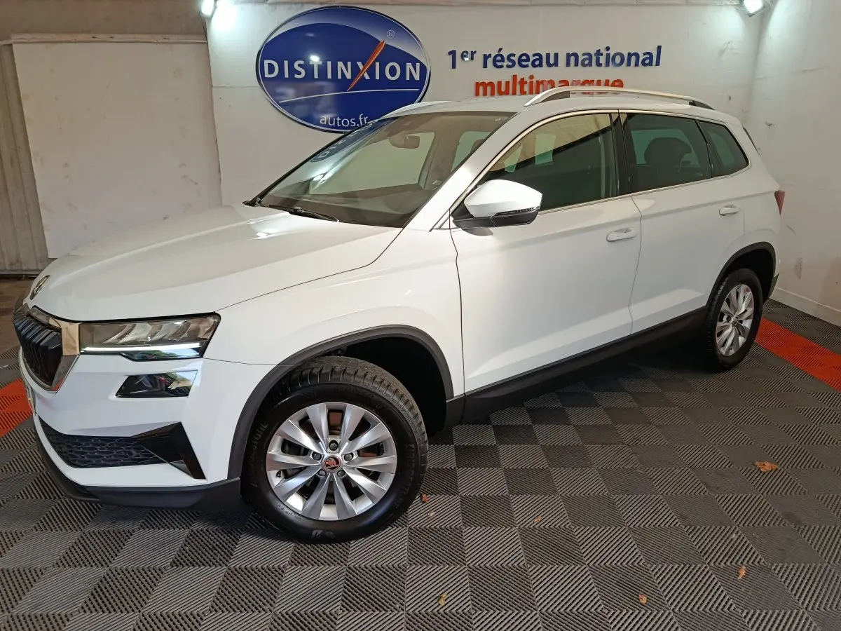 Vue 3/4 avant droit d'un Skoda Karoq blanc 2024 avec jantes alliage et rétroviseurs blancs dans un showroom.