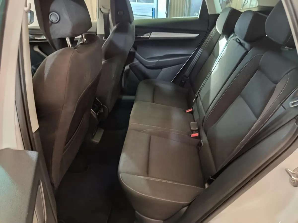 Vue intérieure côté droit montrant la banquette arrière noire du Skoda Karoq blanc 2024 avec ceintures et appuie-têtes.