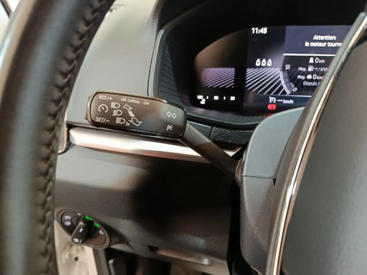 Gros plan sur le commodo gauche et le combiné d'instruments numérique du tableau de bord du Skoda Karoq blanc 2024.