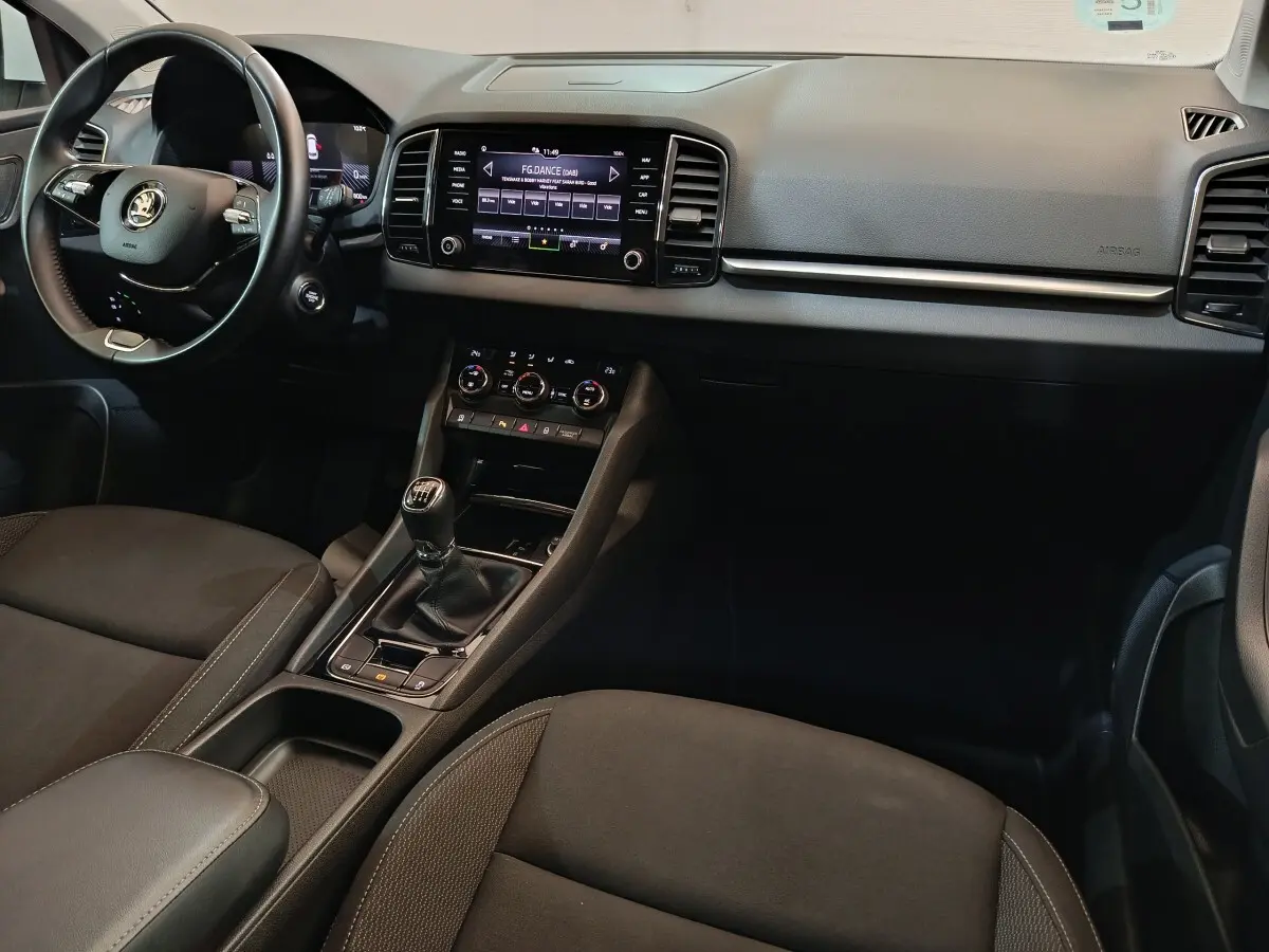 Vue intérieure avant du Skoda Karoq 2.0 TDI 2024, tableau de bord noir avec écran tactile et volant cuir multifonctions.