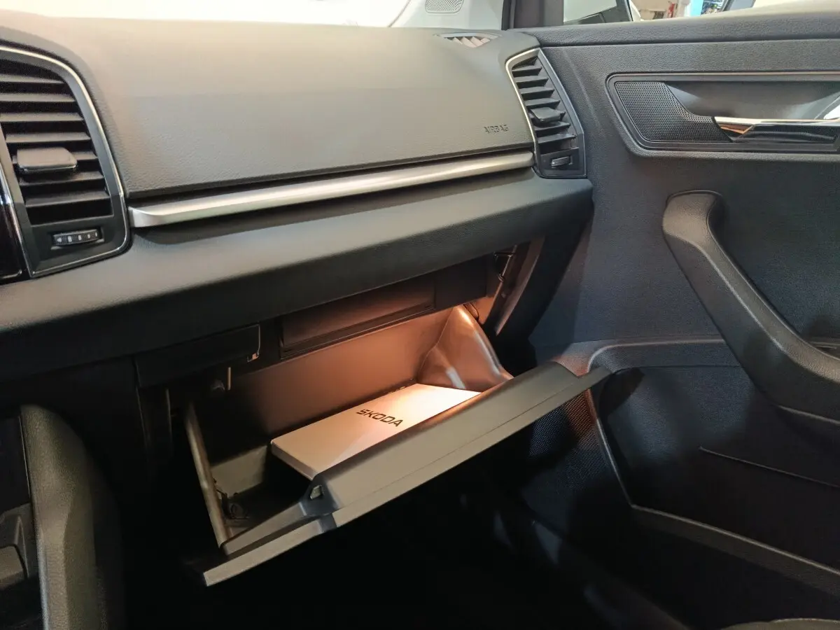Intérieur côté passager du Skoda Karoq 2024, boîte à gants ouverte avec manuel Skoda visible, tableau de bord noir.