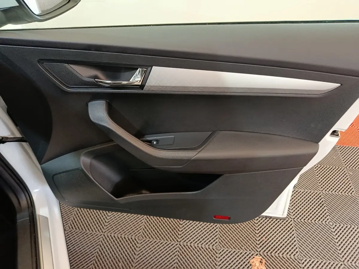 Intérieur côté gauche de la porte avant d’un Skoda Karoq blanc, avec poignée noire et insert décoratif argenté.