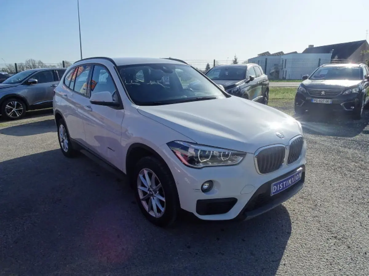 BMW X1 sDrive 18d blanc vue 3/4 avant droit, avec calandre caractéristique et feux LED allumés.