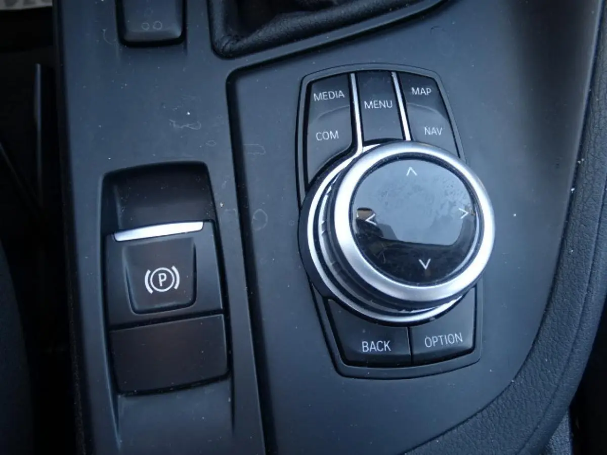 Gros plan sur la molette de commande iDrive et le frein à main électronique dans le BMW X1 sDrive 18d blanc.