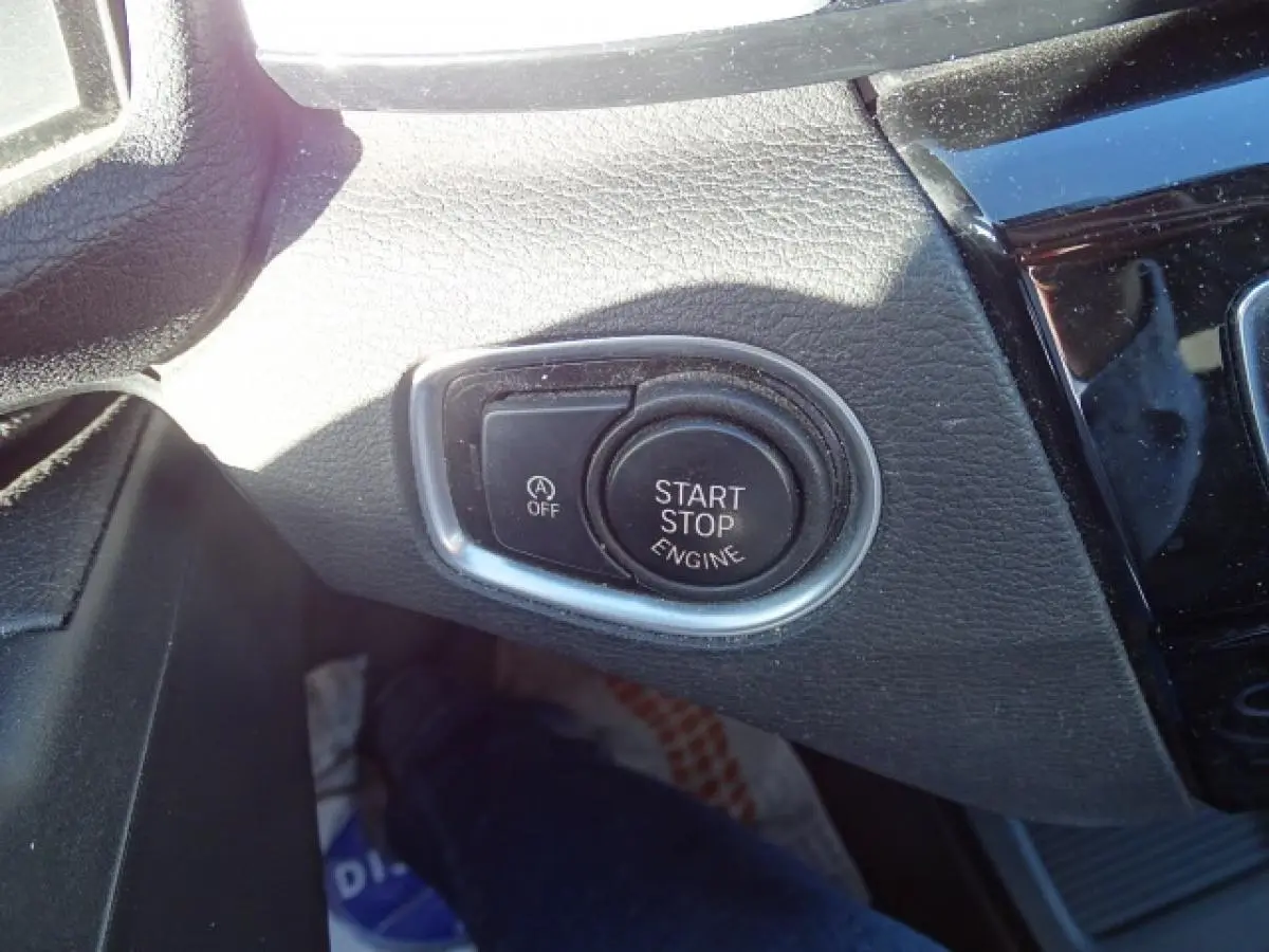 Gros plan sur le bouton Start/Stop moteur entouré de chrome dans l’habitacle noir du BMW X1 blanc 2017.