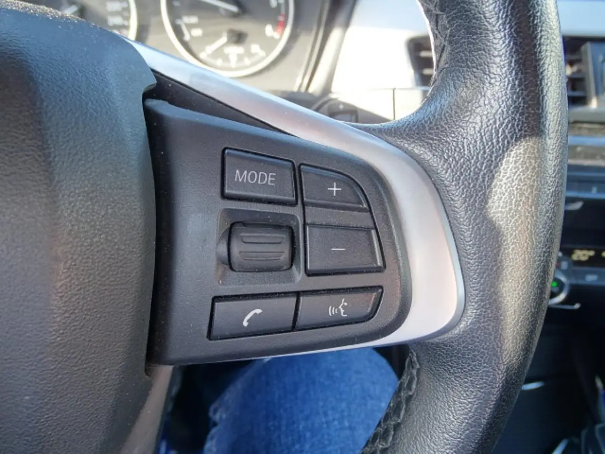 Gros plan sur les commandes multifonctions à gauche du volant cuir noir de la BMW X1 sDrive 18d Business Design 2017.
