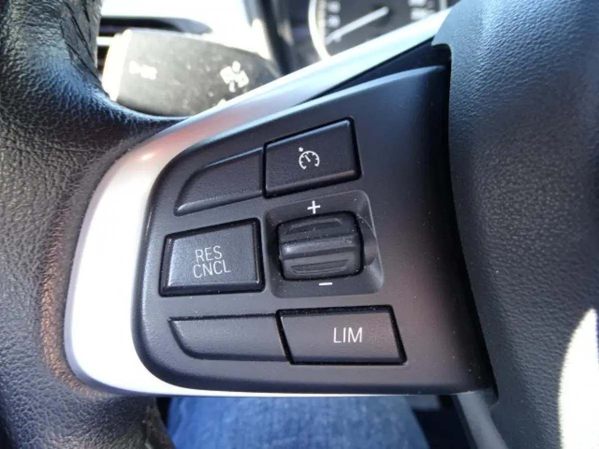 Gros plan sur les commandes de régulateur de vitesse au volant cuir noir du BMW X1 blanc sDrive 18d Business Design.
