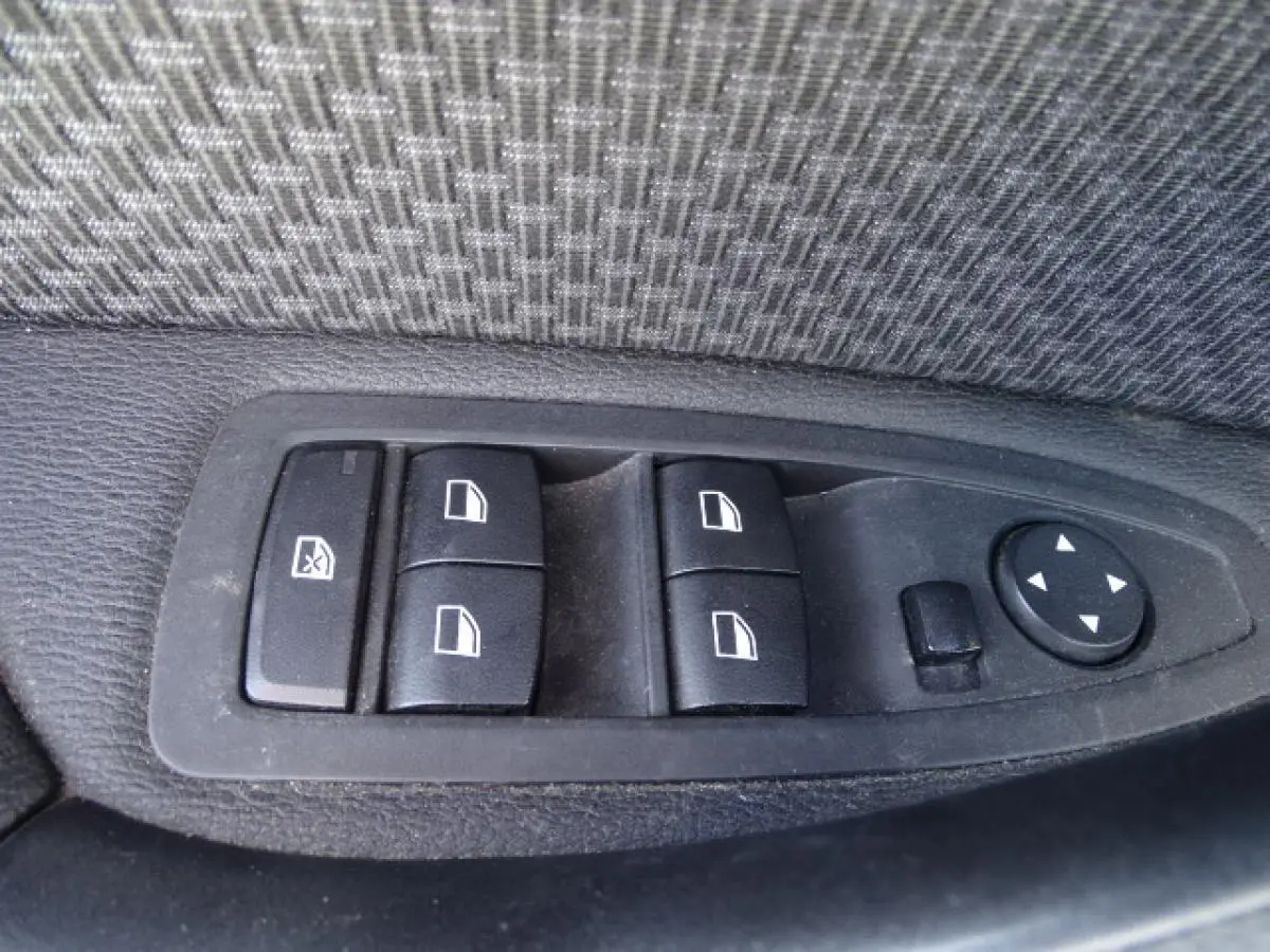 Gros plan sur les commandes de lève-vitres et rétroviseurs côté conducteur d'une BMW X1 blanche de 2017.