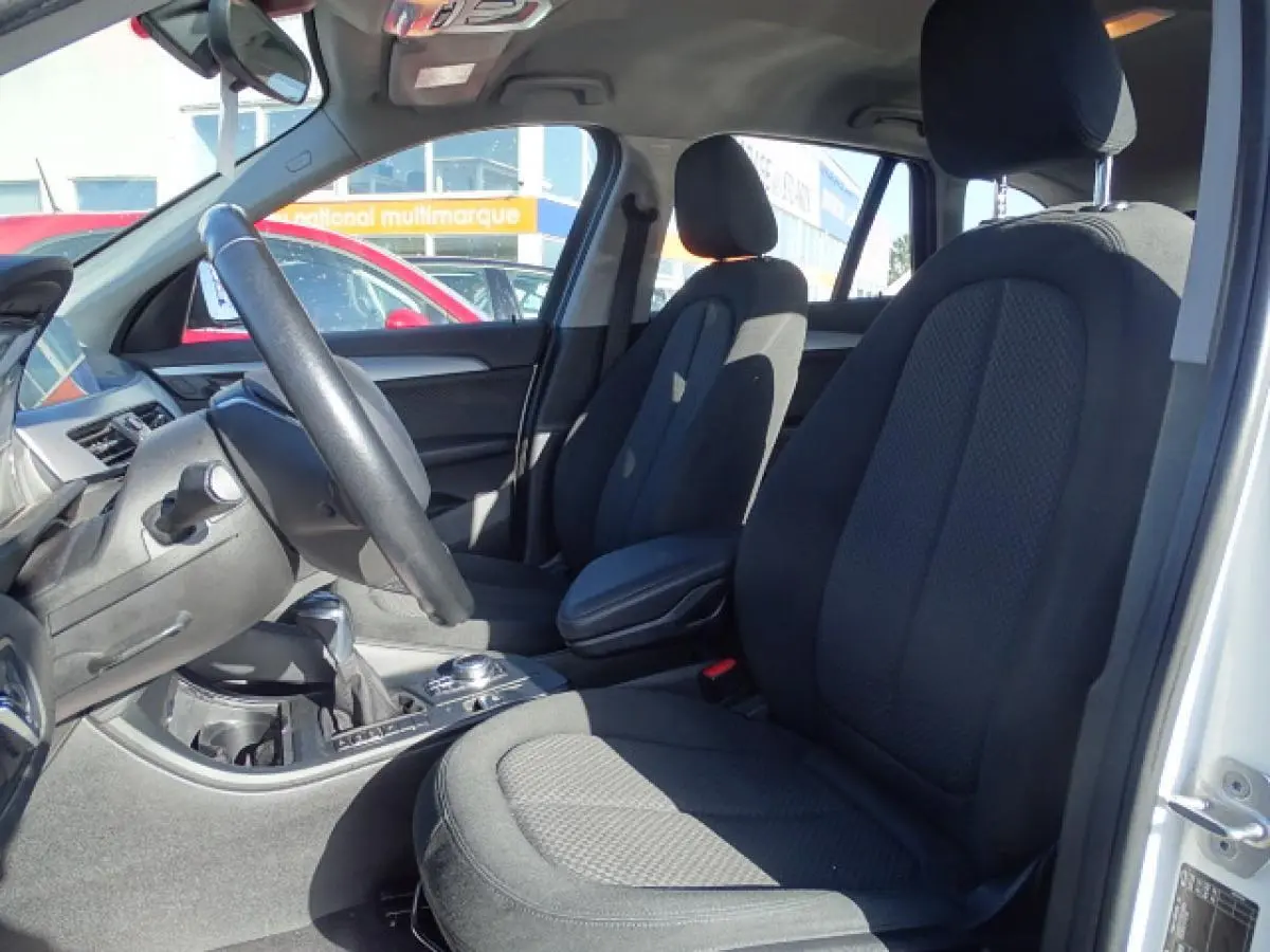 Vue intérieure côté conducteur du BMW X1 blanc 2017, sièges tissu noirs et volant multifonction cuir.