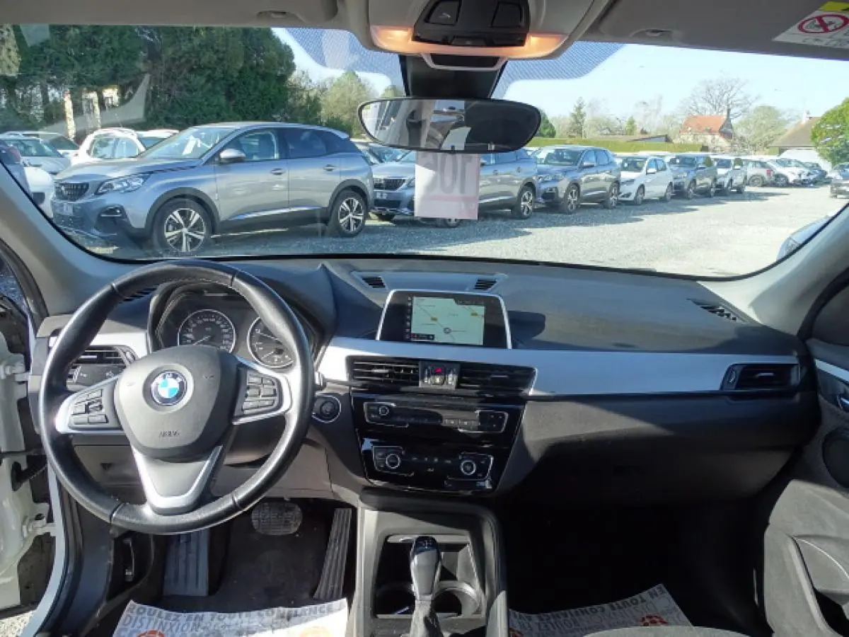 Vue intérieure avant de la BMW X1 blanche 2017, montrant le volant cuir multifonction et l’écran de navigation central.