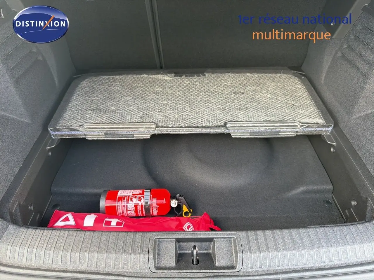 Coffre ouvert d’une Renault Symbioz gris cassiopée, montrant un extincteur rouge et une trousse de secours rouge.