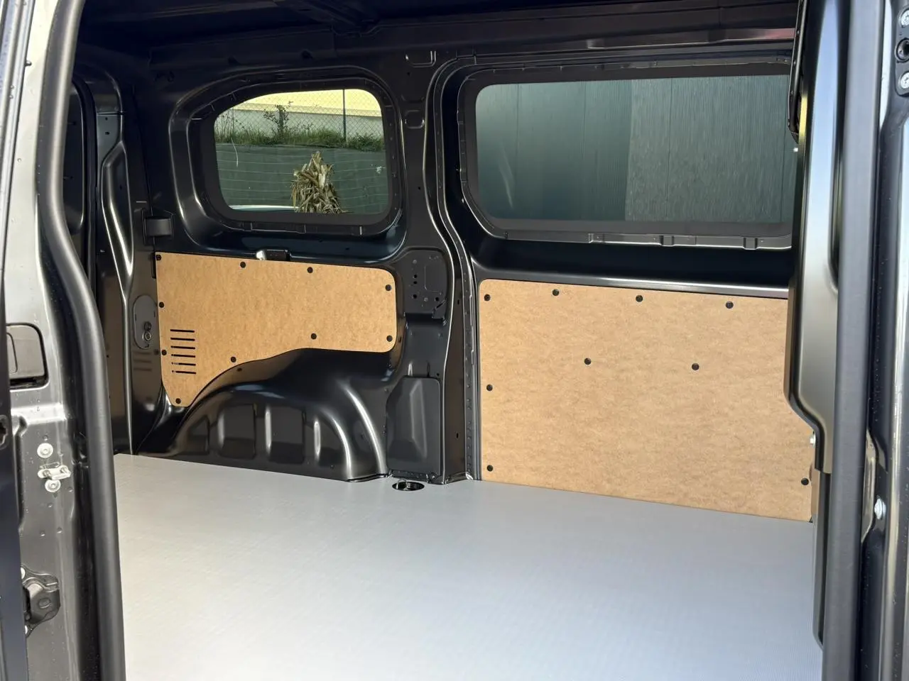 Vue intérieure arrière du Citroën Jumpy gris titane, montrant le plancher bois antidérapant et habillages latéraux en bois.