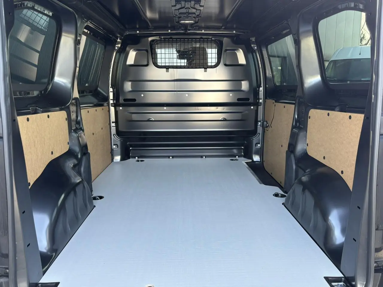 Vue intérieure arrière du Citroën Jumpy gris Titane, montrant le plancher bois antidérapant et la cloison pleine vitrée isolante.