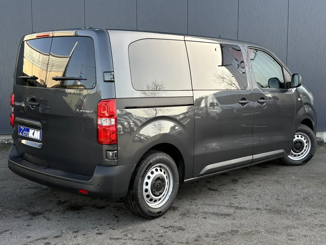 Vue 3/4 arrière droit d'un Citroën Jumpy gris titane avec portes arrière vitrées et jantes acier.