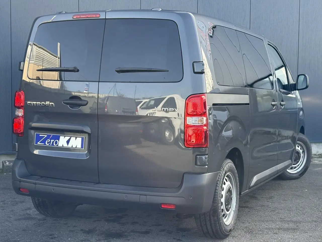 Vue 3/4 arrière droite d'un Citroën Jumpy gris titane avec portes arrière vitrées et plaques Zero KM.
