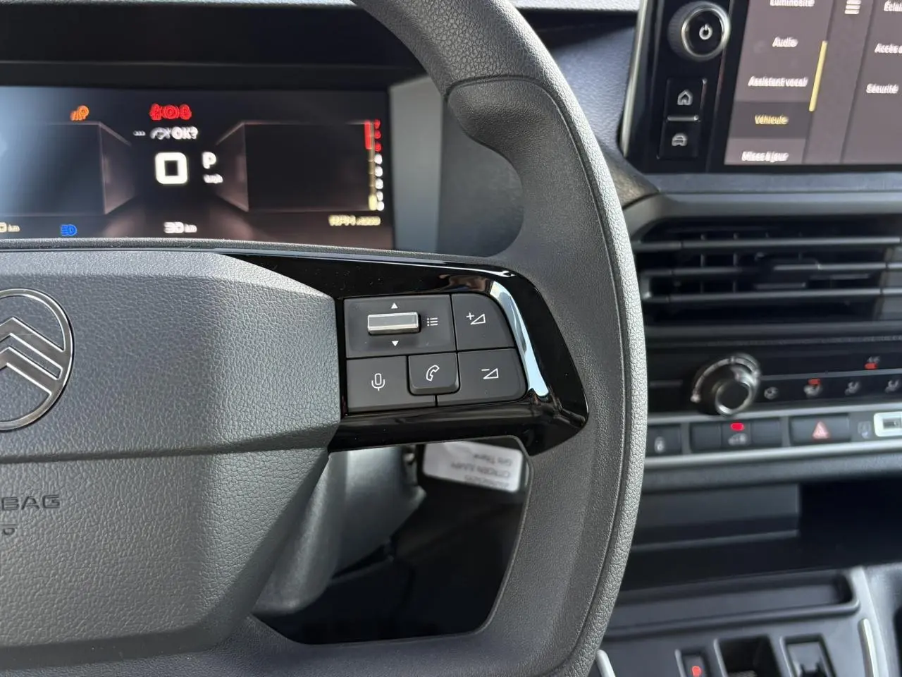 Gros plan sur le volant gris du Citroën Jumpy 2025, avec commandes audio et écran digital en arrière-plan.