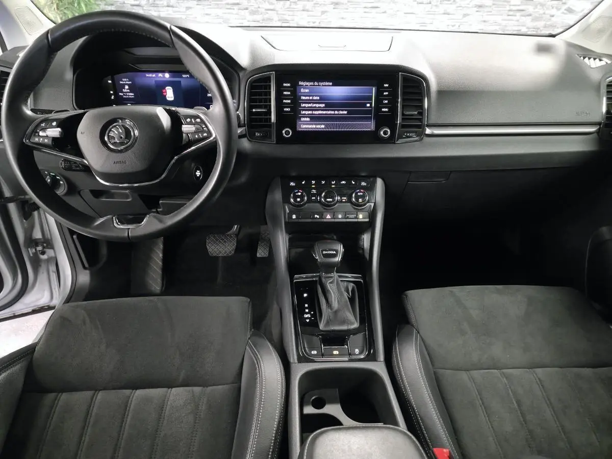 Vue intérieure avant du Skoda Karoq 2023 gris, montrant tableau de bord, volant cuir multifonctions et console centrale avec écran tactile.