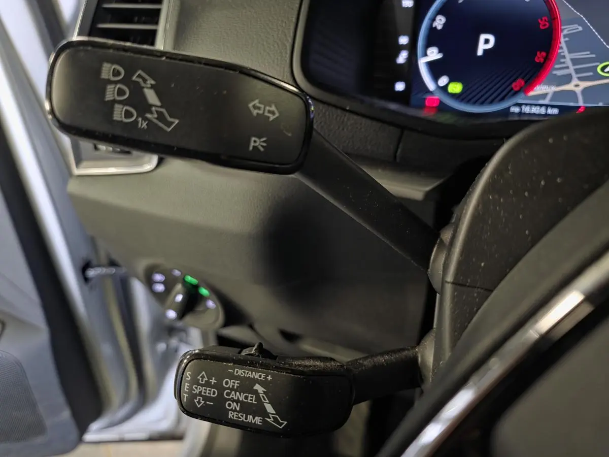 Gros plan sur les commandes au volant du Skoda Karoq 2023, avec affichage numérique et portière grise ouverte en arrière-plan.