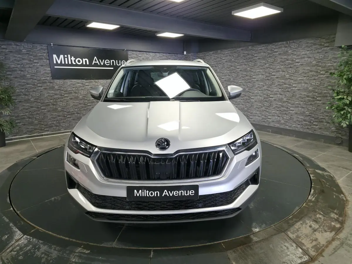 Vue avant d’un Skoda Karoq gris 2023 exposé en showroom avec calandre noire et phares LED distinctifs.