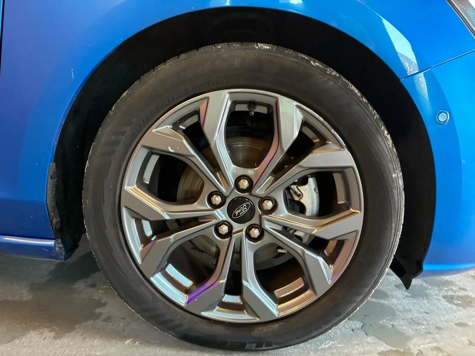 Gros plan sur la roue avant gauche d'une Ford Focus bleu 2024, mettant en valeur la jante alliage au design moderne.