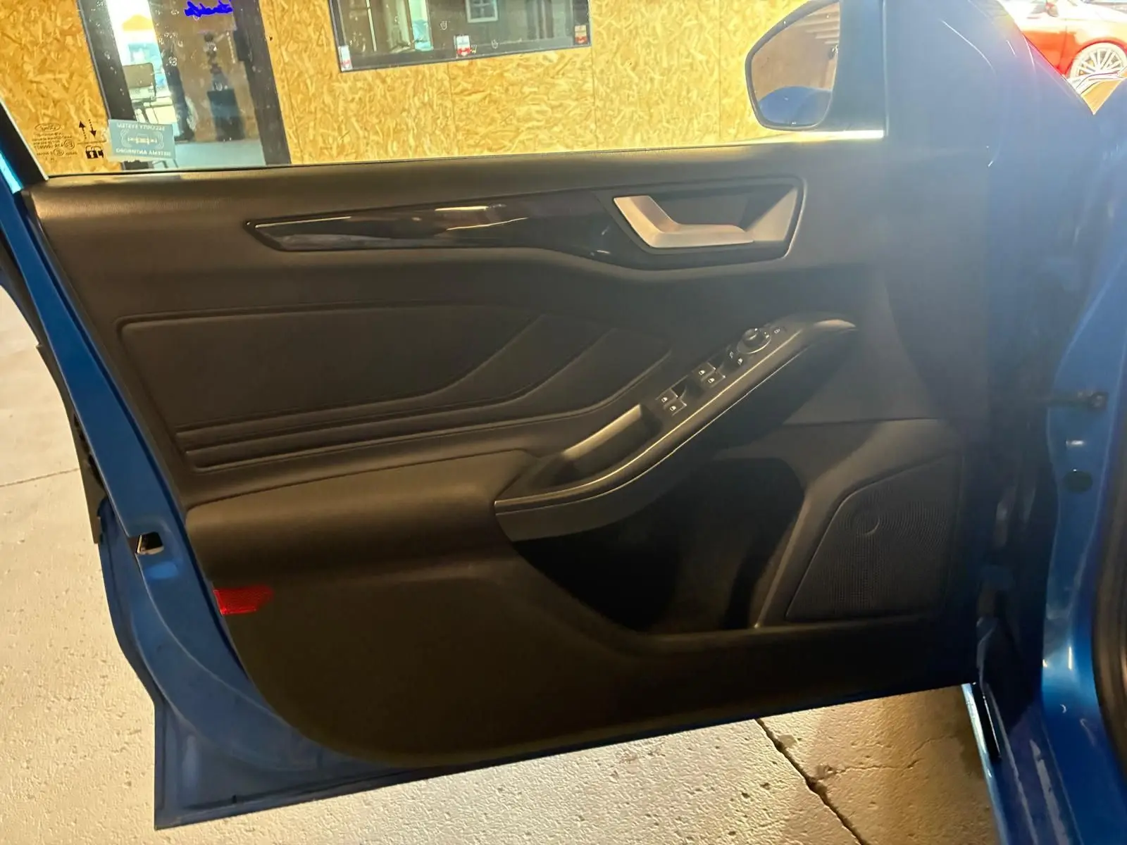 Vue intérieure de la porte avant gauche d’une Ford Focus bleu 2024, avec commandes électriques et garniture noire.