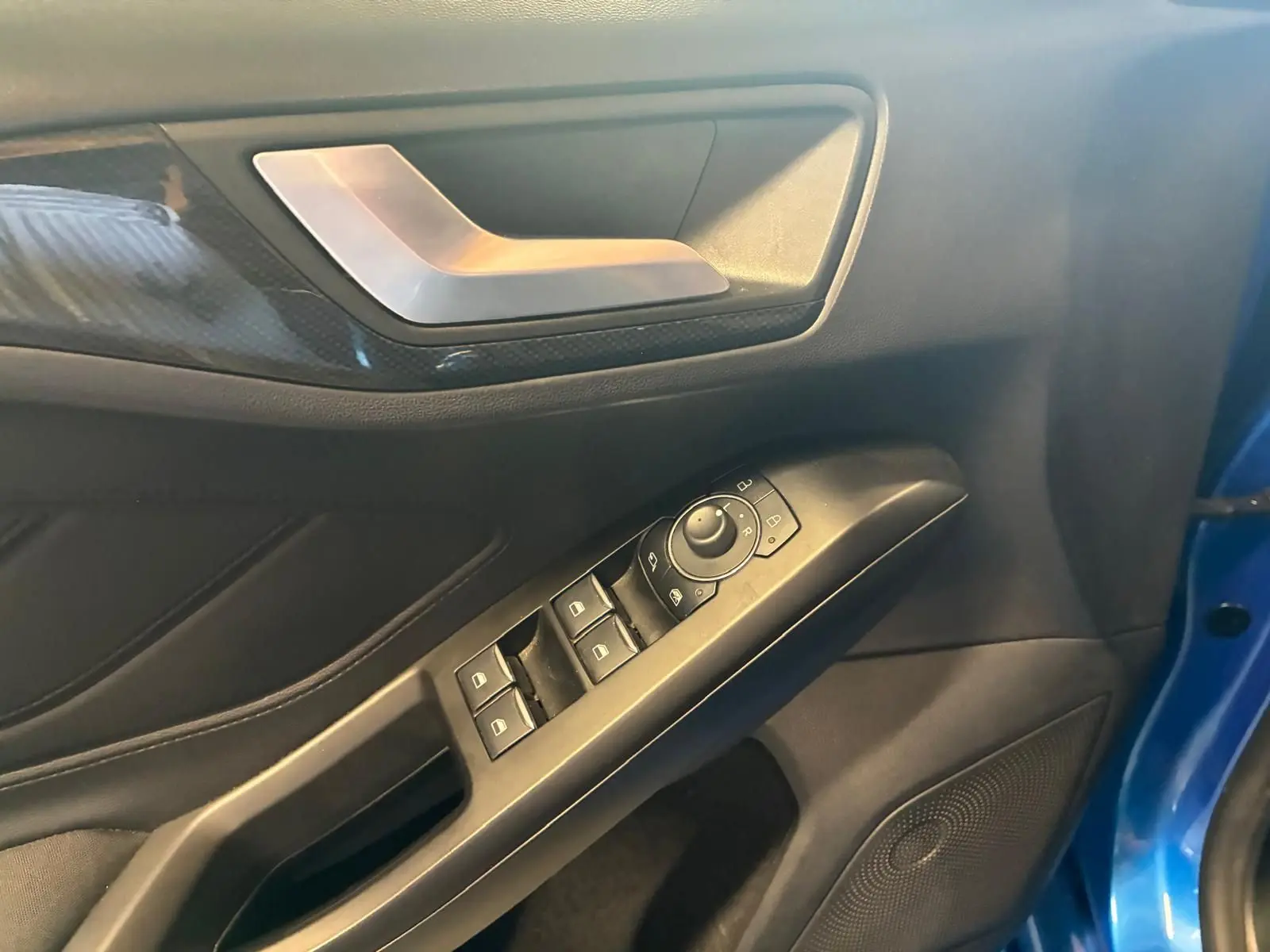 Détail de la porte avant gauche d’une Ford Focus bleue 2024, montrant les commandes des vitres et le revêtement intérieur noir.