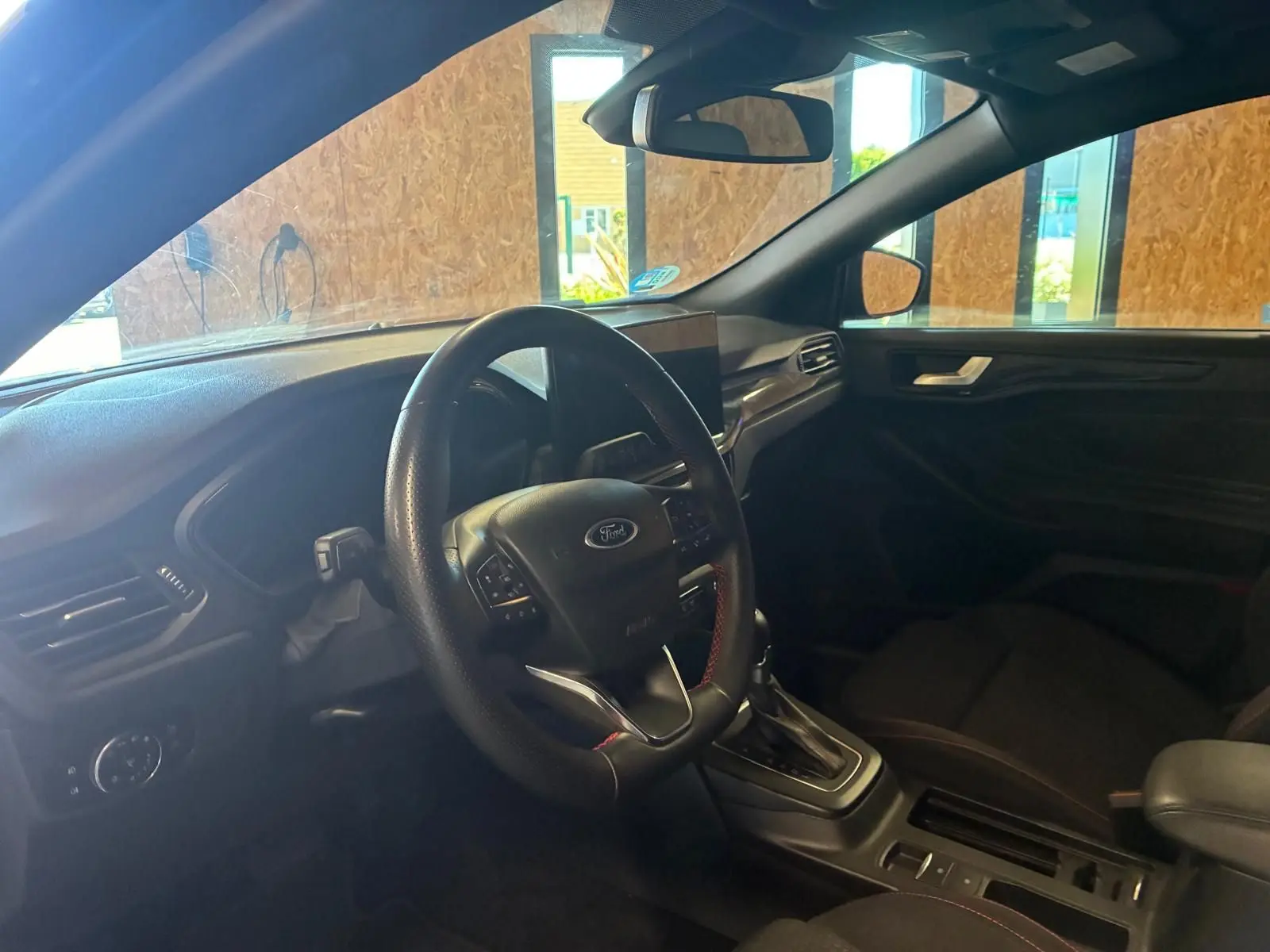 Vue intérieure côté conducteur de la Ford Focus 2024, tableau de bord et volant noir avec surpiqûres rouges.
