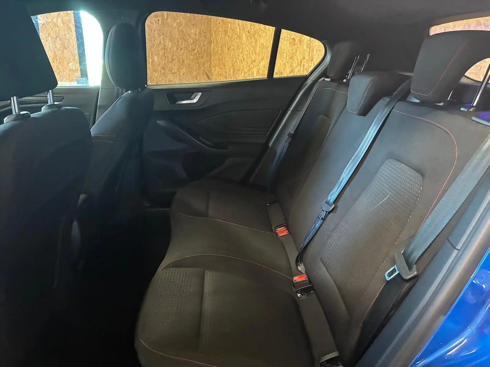 Vue intérieure côté droit des sièges arrière noirs en tissu avec surpiqûres rouges d'une Ford Focus 2024 bleue.