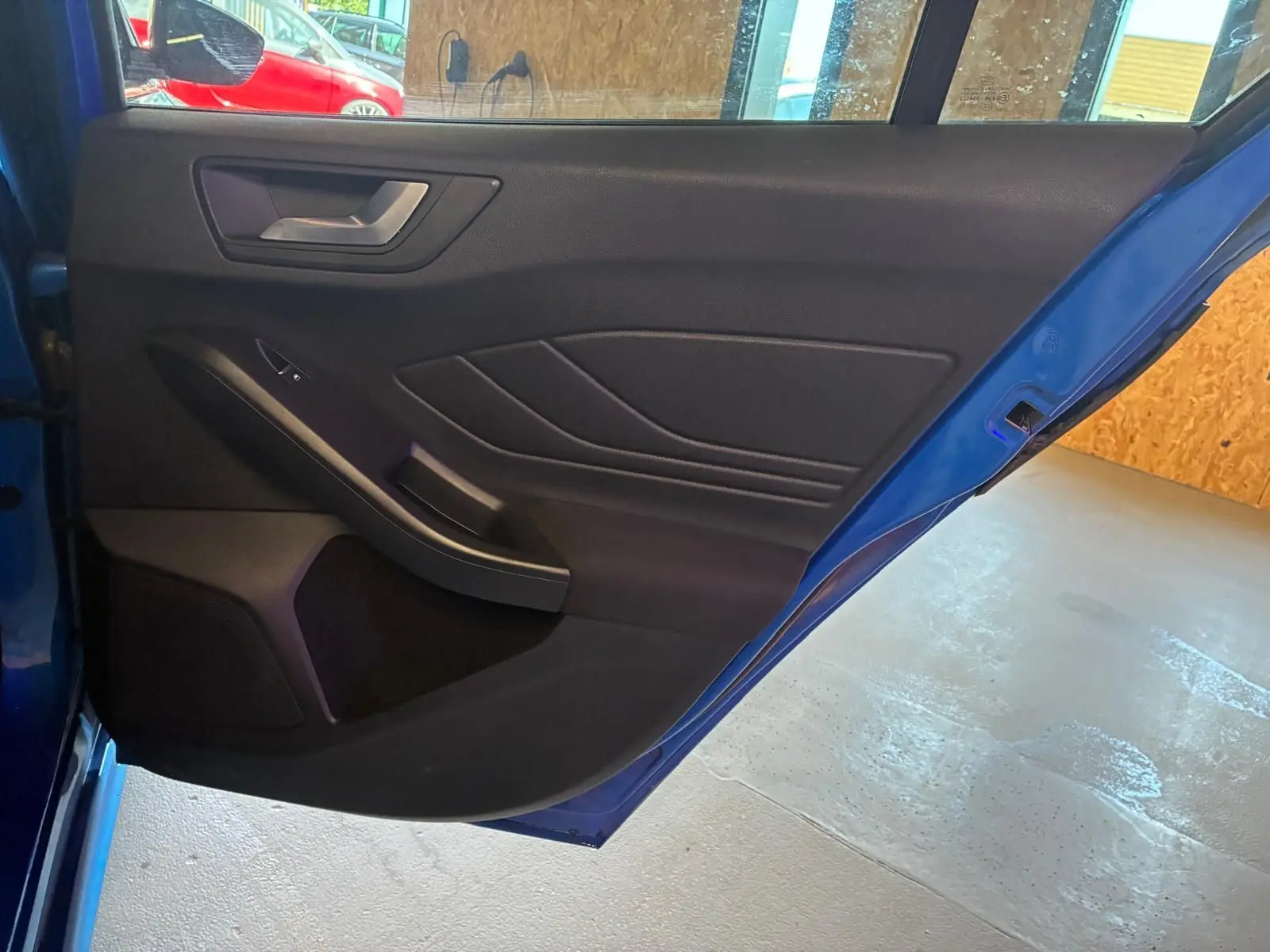 Vue rapprochée de la porte arrière gauche bleu vif d’une Ford Focus 2024, avec garniture intérieure noire et poignée argentée.