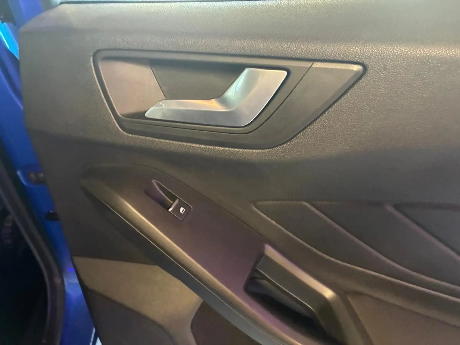 Gros plan sur la poignée intérieure et le bouton de lève-vitre côté gauche d’une Ford Focus bleu 2024.