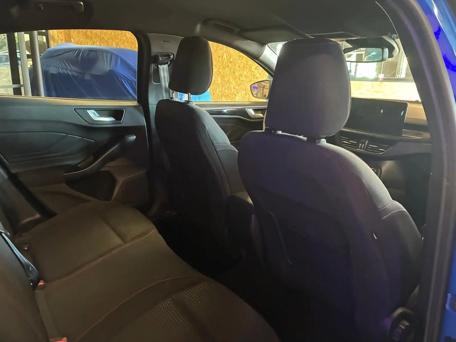 Vue intérieure arrière côté gauche de la Ford Focus 2024 bleu, sièges tissu noirs avec surpiqûres rouges et tableau de bord visible.