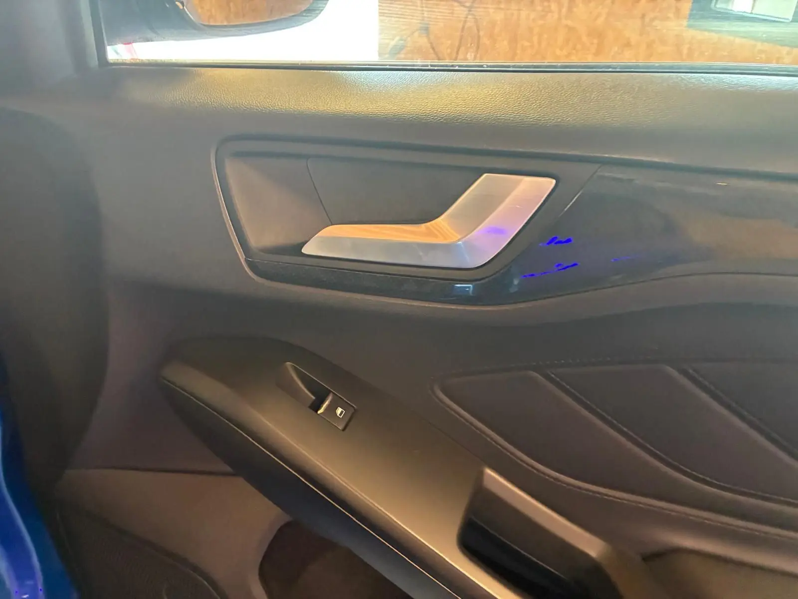 Détail de la porte intérieure côté gauche de la Ford Focus bleu 2024, avec poignée argentée et commande de fenêtre.