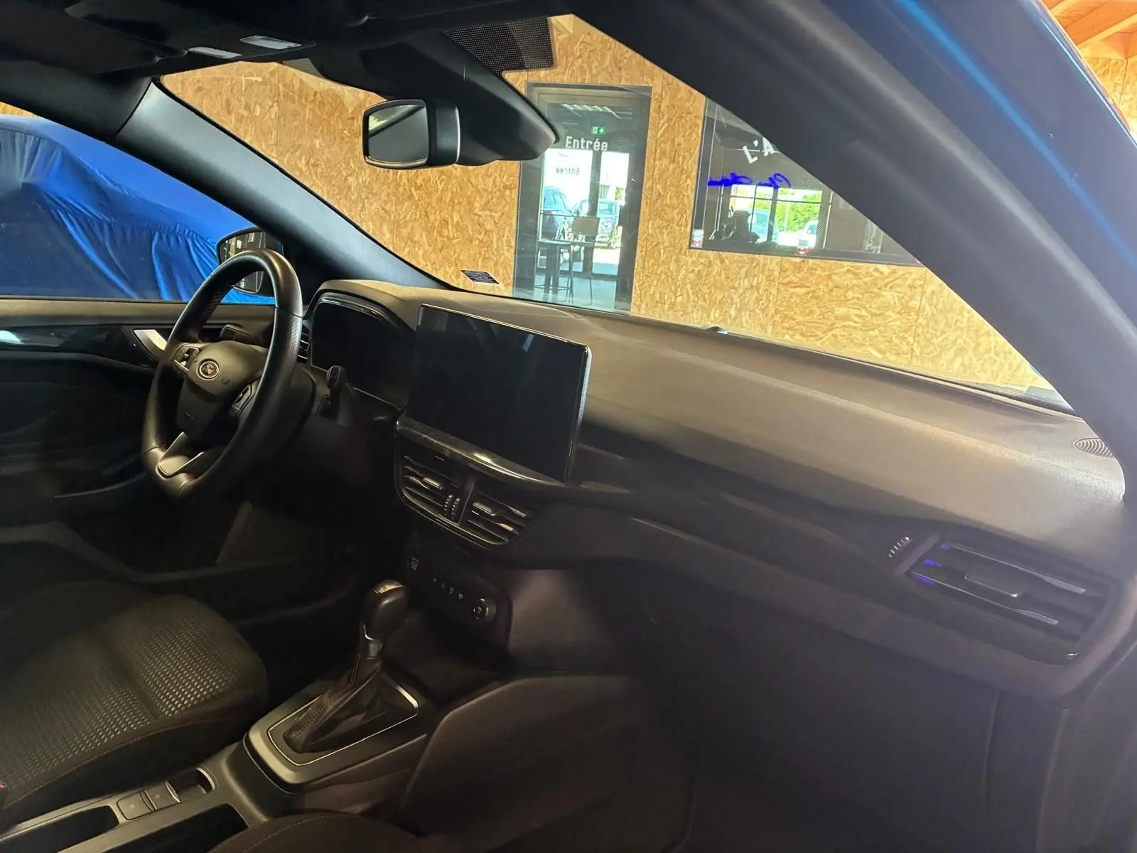 Vue intérieure côté conducteur de la Ford Focus 2024 bleu, montrant le tableau de bord et la console centrale avec écran tactile.