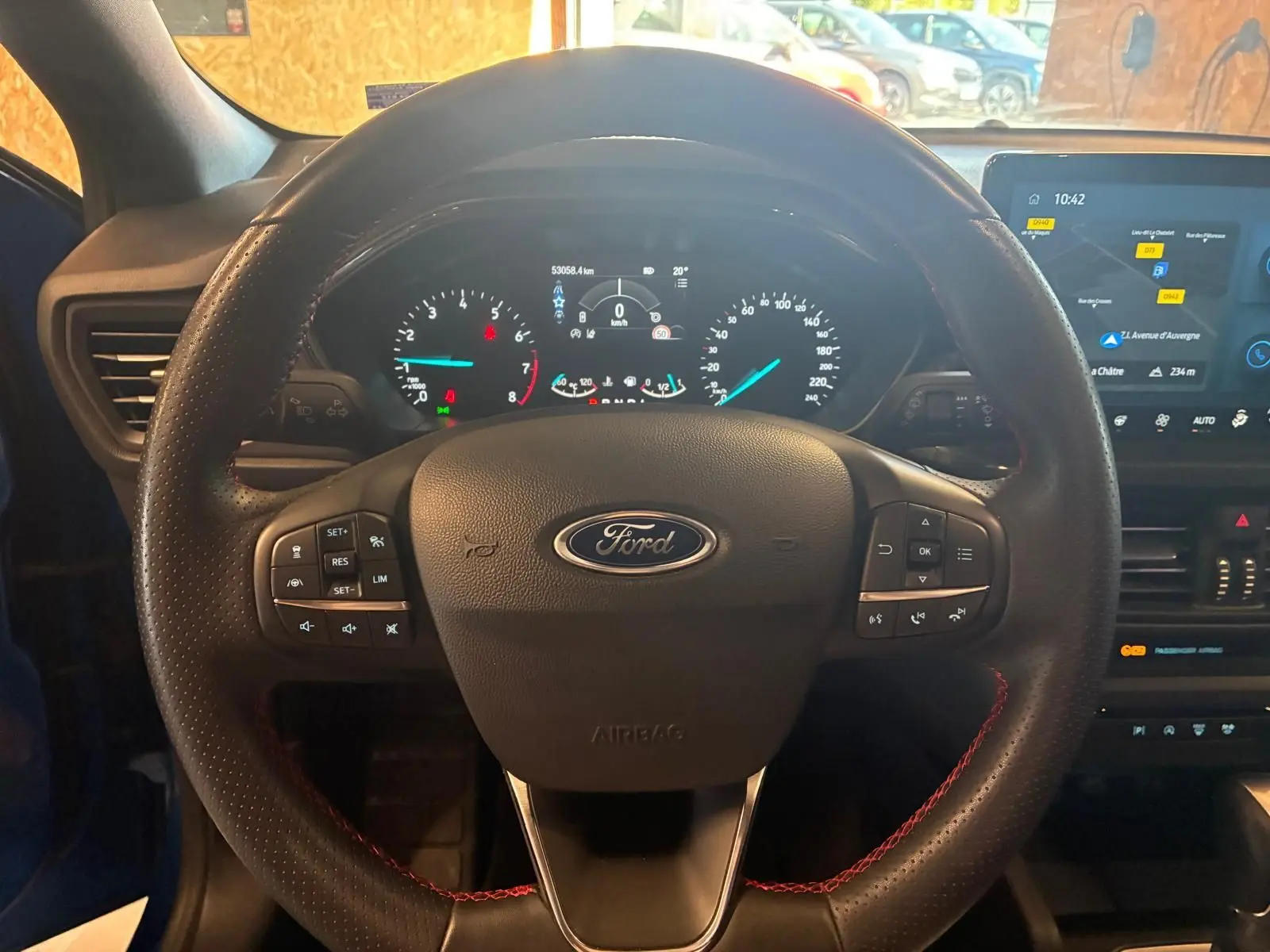 Vue rapprochée du volant noir avec surpiqûres rouges et tableau de bord numérique de la Ford Focus 2024 bleu hybride.