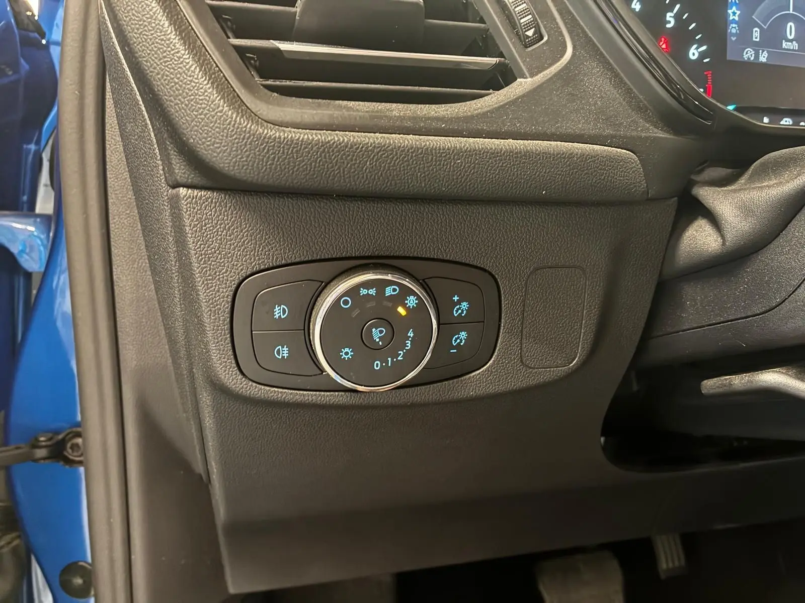 Gros plan sur le panneau de commande des phares à gauche du volant dans l’habitacle noir d’une Ford Focus bleue 2024.