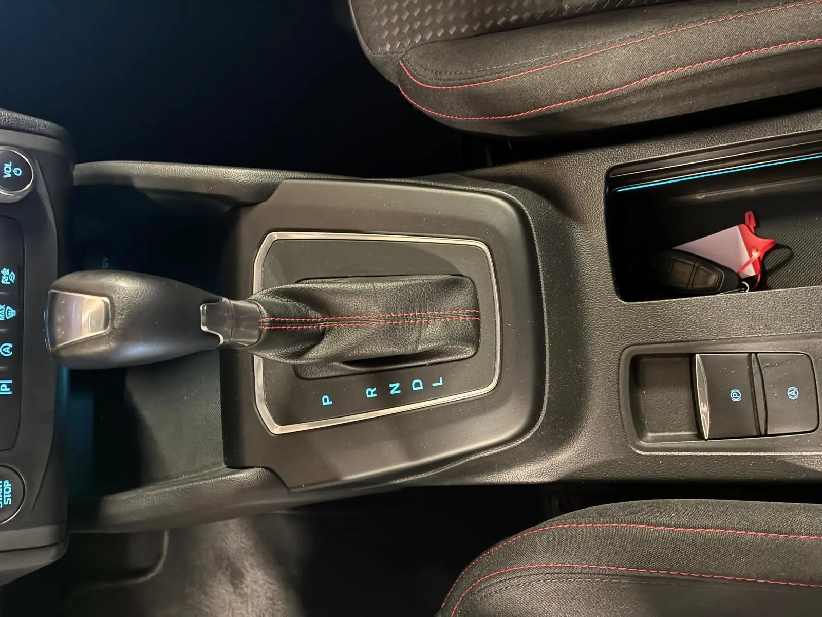 Vue rapprochée de la console centrale d’une Ford Focus bleue 2024, avec levier de vitesse automatique et coutures rouges sur les sièges.