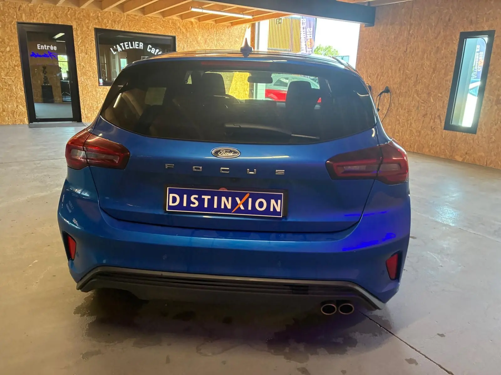 Vue arrière d'une Ford Focus bleu 2024 avec double sortie d'échappement et logo Distinxion visible en intérieur d'atelier.