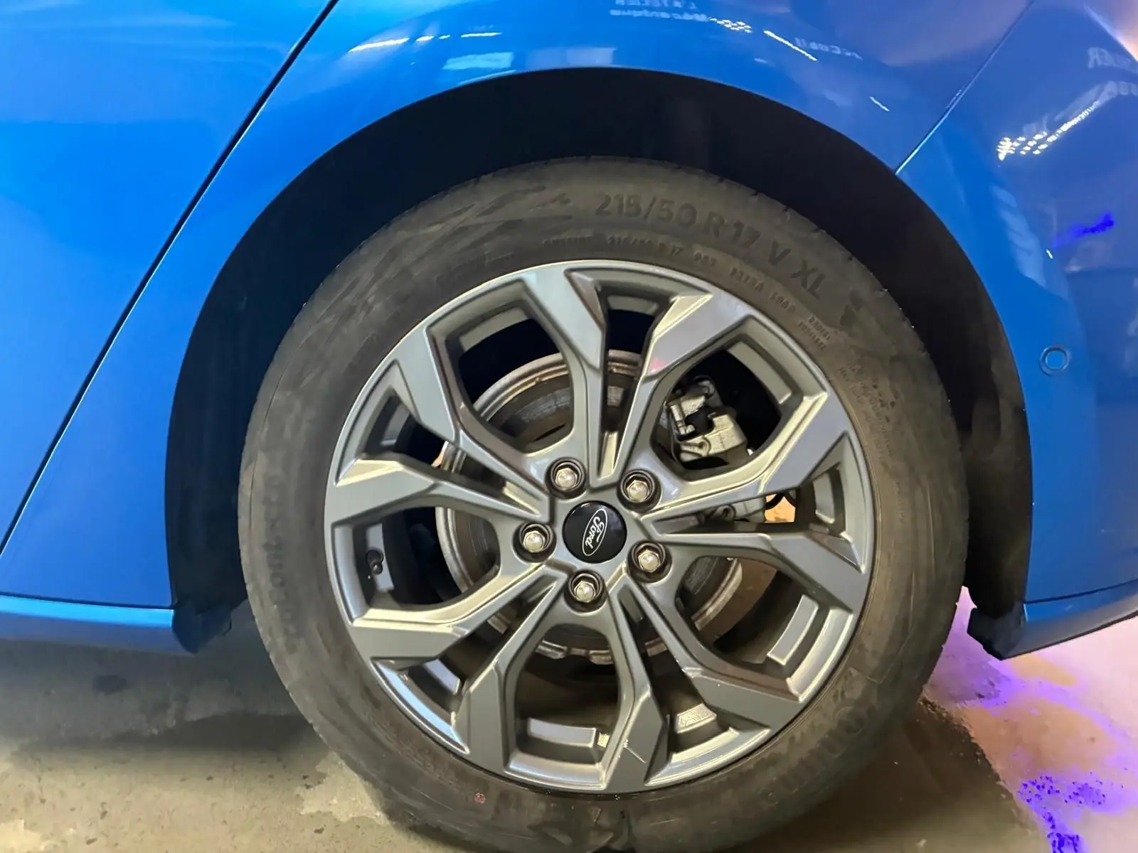 Gros plan sur la roue avant droite d’une Ford Focus bleu vif, mettant en valeur la jante alliage au design moderne.