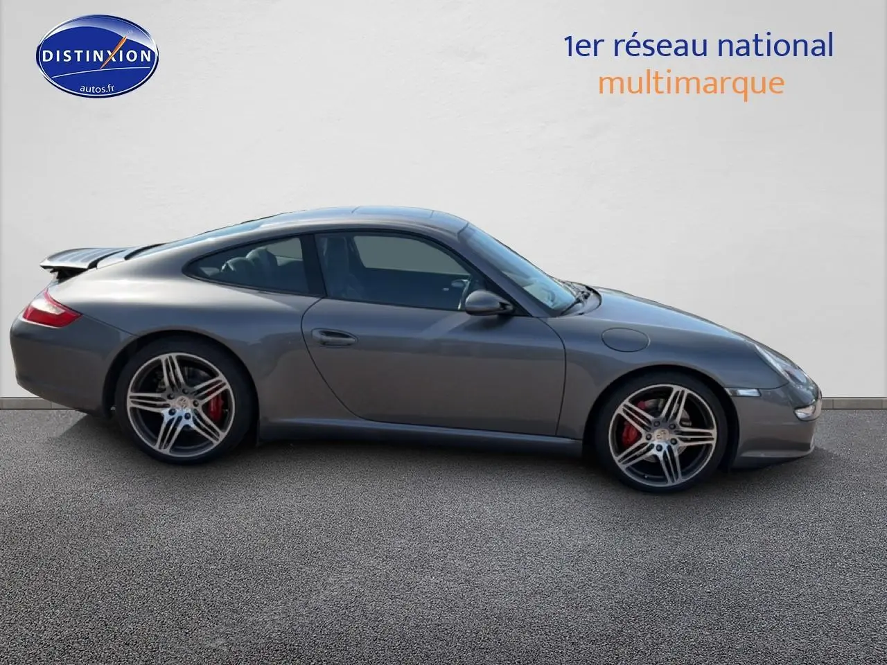 Profil droit d'une Porsche 911 (997) Carrera S gris métallisé avec jantes alu et aileron arrière déployé.