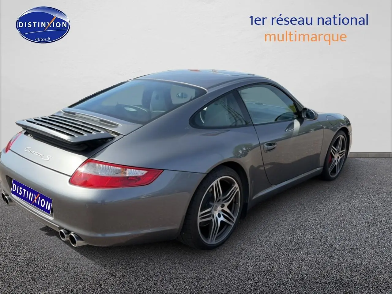 Porsche 911 (997) Carrera S gris vue 3/4 arrière droit, jantes alu et aileron arrière déployé.