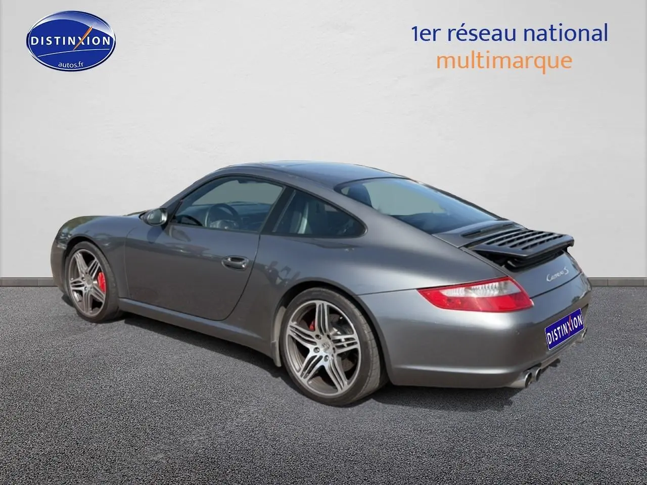 Porsche 911 (997) Carrera S gris vue 3/4 arrière droit, avec jantes alu et aileron arrière déployé.