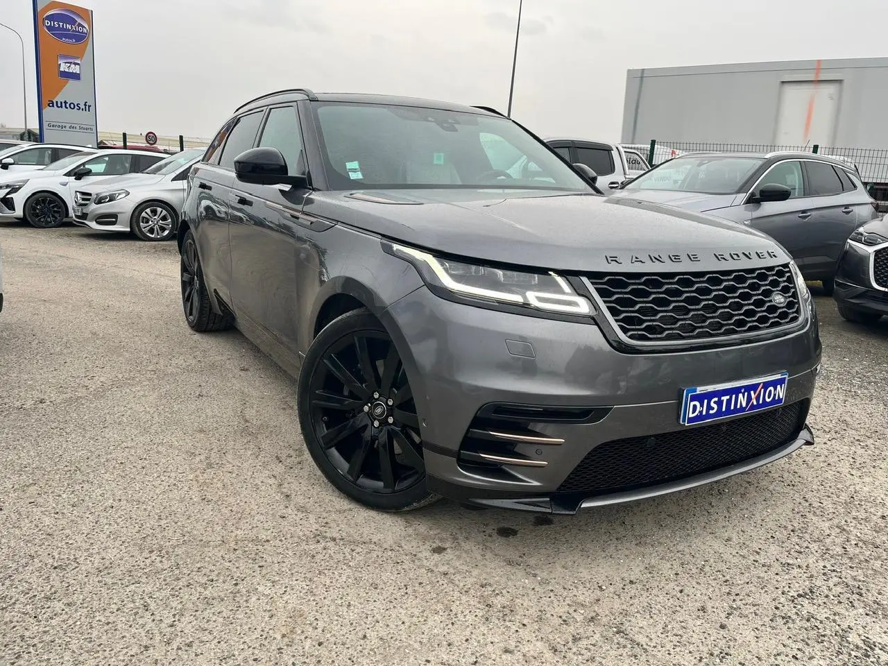 Range Rover Velar gris ammonite en 3/4 avant droit avec jantes noires 21 pouces et calandre hexagonale distinctive.
