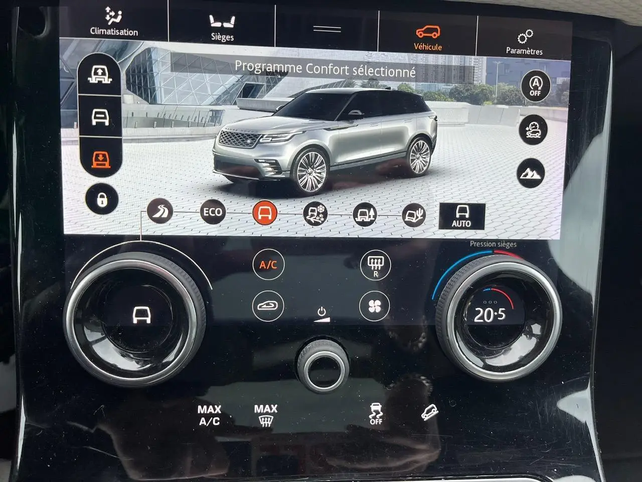 Écran tactile intérieur montrant un Range Rover Velar gris ammonite en vue 3/4 avant avec options de conduite et climatisation.