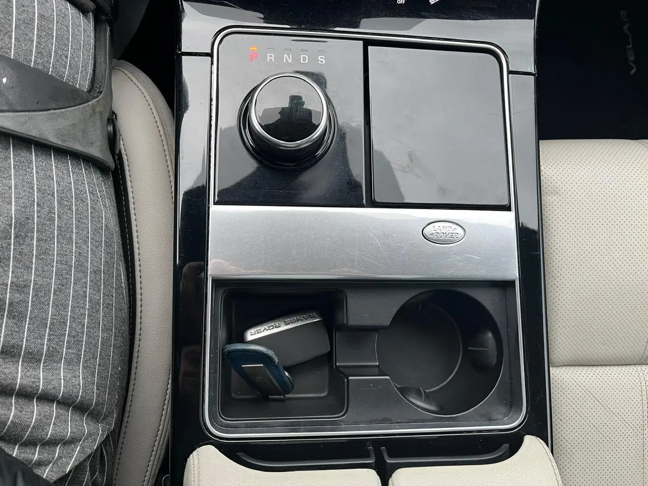 Vue plongeante sur la console centrale noire brillante du Range Rover Velar gris Ammonite avec clé Loisirs et porte-gobelet.
