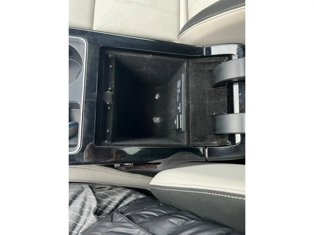 Vue rapprochée de la console centrale ouverte du Range Rover Velar, avec accoudoir en cuir beige et finition noire brillante.