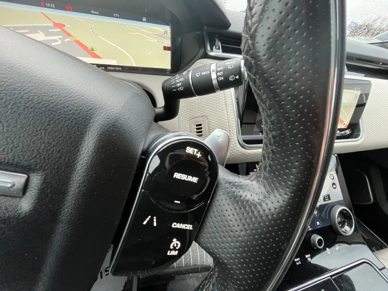 Gros plan sur le volant en cuir perforé noir du Range Rover Velar 2017, avec commandes de régulateur et écran de navigation visible.