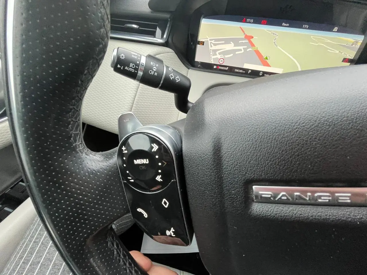 Gros plan sur le volant noir perforé du Range Rover Velar 2017, avec commandes intégrées et écran de navigation visible en arrière-plan.