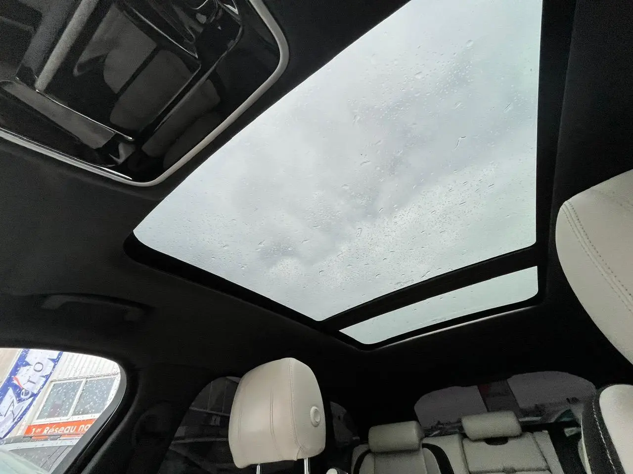 Vue intérieure du toit ouvrant panoramique et des sièges clairs du Range Rover Velar gris Ammonite, ambiance lumineuse naturelle.